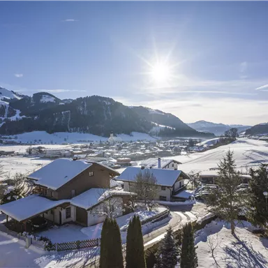 A wintry landscape with snow-covered mountains and shining sunlight. Small houses lie in an idyllic, snowy valley.