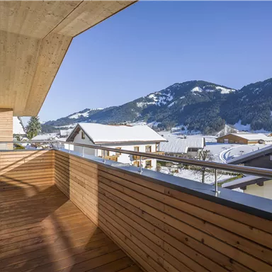 A balcony with wooden paneling and a view of snow-covered mountains. The clear blue sky completes the winter landscape.