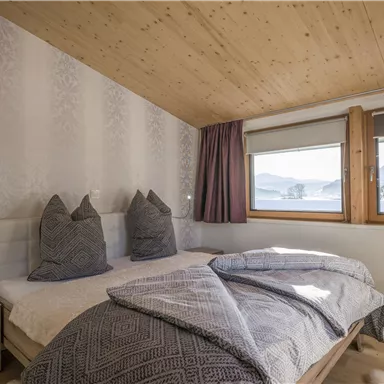 A cozy bedroom with a double bed and two large pillows. Through the windows, one has a view of the mountains and the surrounding landscape.