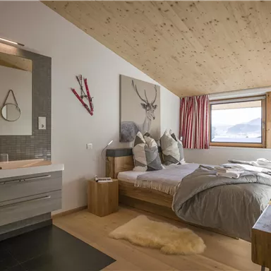 A cozy bedroom with a double bed and a modern bathroom. Large windows offer a view of the mountains and let in plenty of daylight.