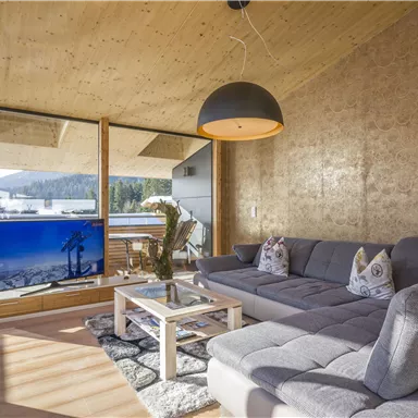 A modern living room with large windows and plenty of natural light. The space is simply furnished, with a cozy couch and a television.