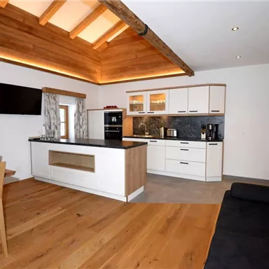 Eine moderne Küche mit Holzdetails und einem Essbereich. Der Raum ist hell und freundlich mit großen Fenstern.