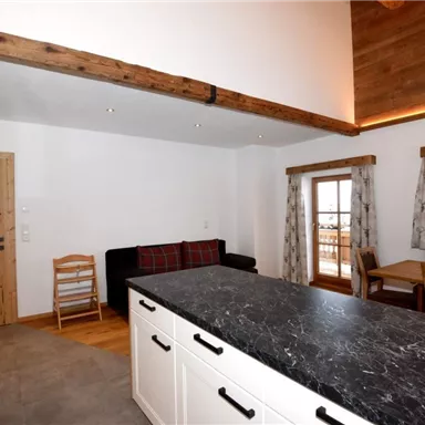 Eine moderne Küche mit einem großen schwarzen Arbeitsbereich und Holzdetails. Der Raum ist hell und freundlich mit einem Esstisch und einem gemütlichen Sitzbereich.