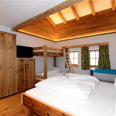 Ein gemütliches Schlafzimmer mit einem Etagenbett und einem großen Bett. Holzmobiliar und ein moderner Stil schaffen eine einladende Atmosphäre.