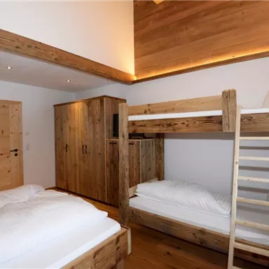 Ein gemütliches Zimmer mit Holzmöbeln und einem Hochbett. Es gibt ein Einzelbett und einen Schrank, dazu eine helle Atmosphäre.