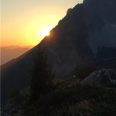 A sunset behind a majestic mountain. The landscape is surrounded by gentle hills and trees.