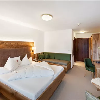 A modern hotel room with a double bed and a cozy seating area. Wooden elements give the space an inviting atmosphere.
