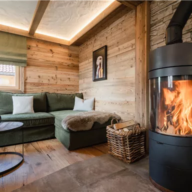 Ein gemütlicher Wohnraum mit einer grünen Couch und einem modernen Kamin. Die Holzvertäfelung und sanfte Beleuchtung sorgen für eine warme Atmosphäre.