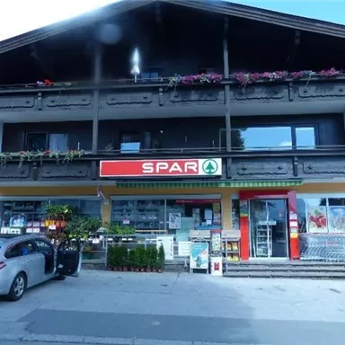 A supermarket with the logo "SPAR" is located in a traditional building. In front of the store, some plants and goods are displayed.