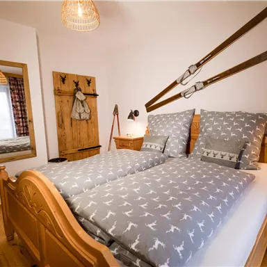 Ein gemütliches Schlafzimmer mit zwei Betten und traditionellen Holzmöbeln. Die Wände sind mit Skiern dekoriert, und ein großer Spiegel reflektiert den Raum.