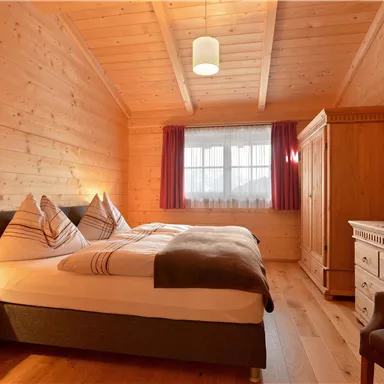A cozy bedroom with wooden paneling and a double bed. The room is bright and features a television and a wardrobe.