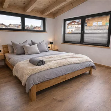 Ein gemütliches Schlafzimmer mit einem Holzbett und weichen Kissen. Große Fenster bieten einen Blick auf die Umgebung und lassen viel Licht herein.