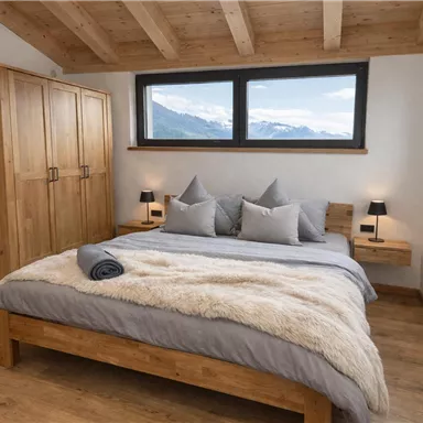 Ein modernes Schlafzimmer mit einem großen Bett und Holzdekor. Große Fenster bieten einen Blick auf die Berge.