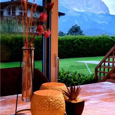 A cozy table with decorative vases and plants. In the background, the impressive mountains and a green landscape can be seen.