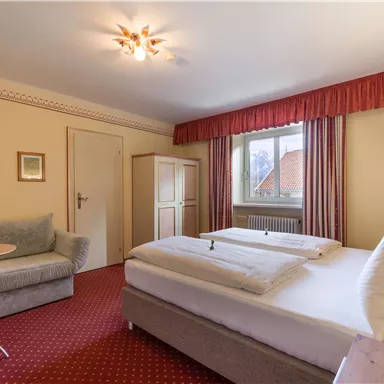 Ein gemütliches Hotelzimmer mit einem großen Bett und einem kleinen Tisch. Die Wände sind in sanften Farben gehalten und ein Fenster sorgt für Tageslicht.