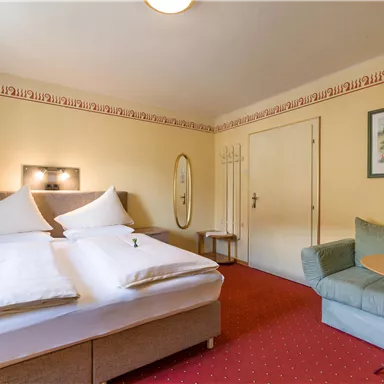 Ein gemütliches Hotelzimmer mit einem großen Doppelbett und einer Sitzecke. Die Wände sind in warmen Farben gehalten, und ein Bild hängt dekorativ an der Wand.