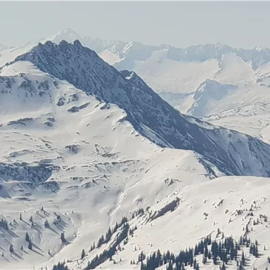 An impressive mountain panorama with snow-covered peaks. In the background, further mountains and a clear, frosty atmosphere can be seen.