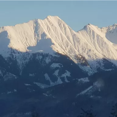 Snow-covered mountains under a clear sky. The majestic peaks cast long shadows into the valley.