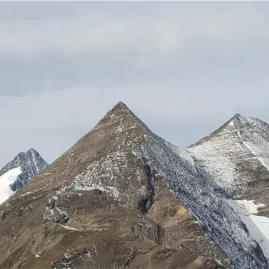 The image shows majestic mountains with snow-capped peaks. The sky is slightly cloudy.