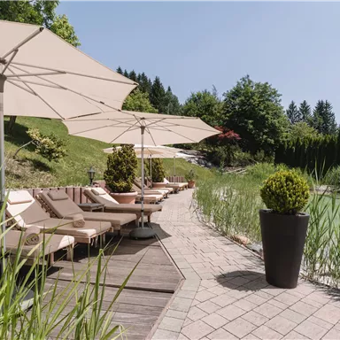 Ein einladender Außenbereich mit Liegen und Sonnenschirmen. Umgeben von grünen Pflanzen und einem ruhigen Ambiente.