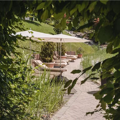 Ein schöner Gartenweg mit Liegen und Sonnenschirmen. Umgeben von üppigem Grün und Pflanzen.