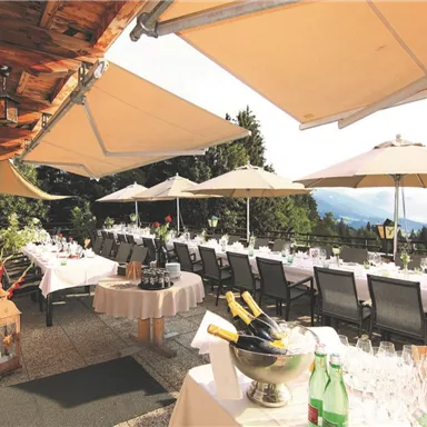 Eine elegante Terrasse mit Tischen, umgeben von Sonnenschirmen und grüner Natur. Ideal für Veranstaltungen oder entspannte Zusammenkünfte im Freien.