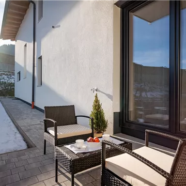 A cozy terrace with modern garden furniture and a beautiful view. The sun is shining on the snow-covered ground.