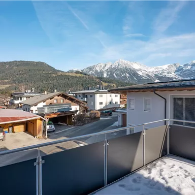 A beautiful view of snow-covered mountains and a picturesque alpine landscape. The sun shines over the rooftops of the houses in the area.