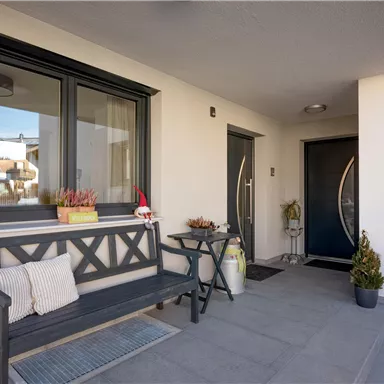 A modern entrance area with a bench and decorative plants. The walls are light, and the windows have a beautiful frame color.