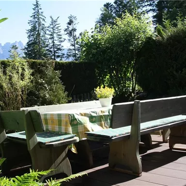 Ein einladender Gartentisch aus Holz mit Bänken steht im Freien. Umgeben von grünen Pflanzen und einem sonnigen Himmel bietet der Platz eine gemütliche Atmosphäre.