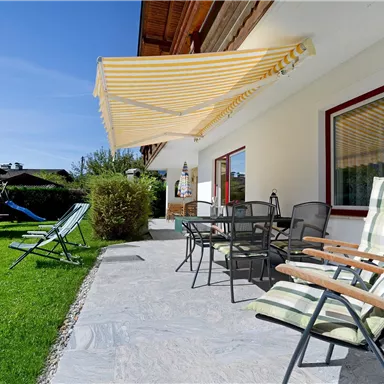 Eine einladende Terrasse mit Gartenmöbeln und Sonnenschirm. Grüne Wiese und ein schöner Ausblick sorgen für Entspannung.