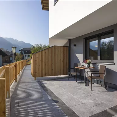 A modern terrace with a table and two chairs. In the background, mountains and houses can be seen.