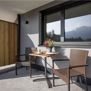 A modern balcony with a small table and two chairs. On the table are a cup and a flower vase.
