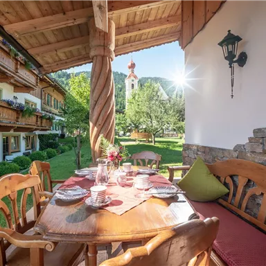 An inviting dining table on a terrace overlooking a garden. In the background, traditional buildings and a church are visible.