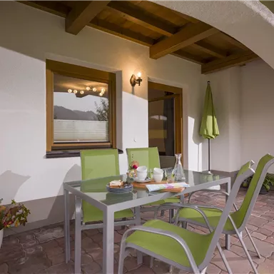 An inviting patio with a glass table and green chairs. In the background, there are windows and a green awning.