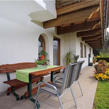 A cozy outdoor area with a table and chairs. Surrounded by flowers and a well-maintained lawn.