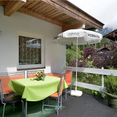 A cozy balcony with a green table and orange chairs. A parasol is ready, while plants beautify the surroundings.