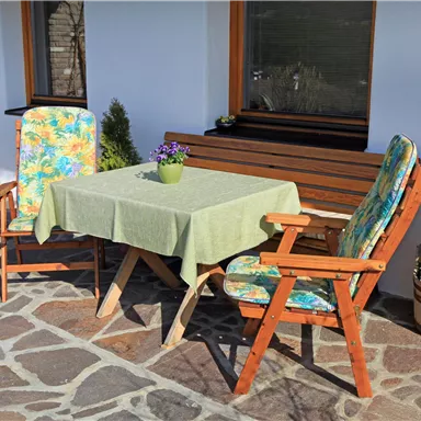 Ein gemütlicher Außenbereich mit einem Tisch und zwei Stühlen. Auf dem Tisch steht ein Pflanzenarrangement, und die Umgebung ist hell und einladend.