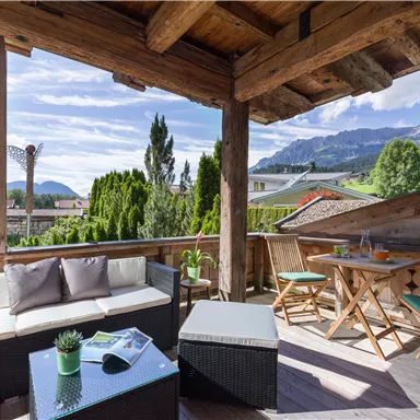 A cozy terrace with wood paneling and a view of the mountains. There is a seating area and a table with chairs to enjoy the scenery.