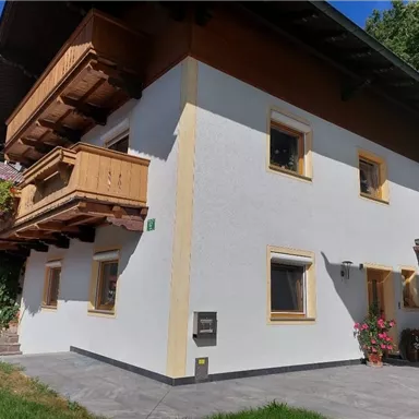 Ein modernes, zweigeschossiges Haus mit Holzbalkonen und hellen Wänden. Der Außenbereich ist gepflegt mit grüner Rasenfläche und Pflanzen.