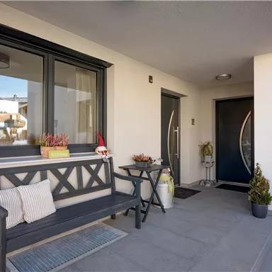 A modern entrance area with a bench and decorative plants. The walls are light, and the windows have a beautiful frame color.