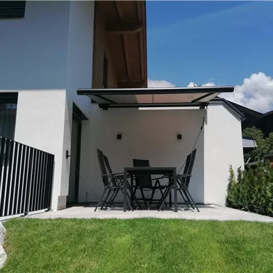 Eine moderne Terrasse mit einem Esstisch und Stühlen. Im Hintergrund sind grünes Gras und eine entspannte Wohnatmosphäre zu sehen.