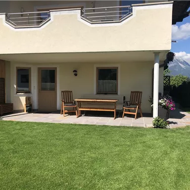 A cozy terrace with wooden furniture and a well-kept lawn. The mountains are visible in the background.