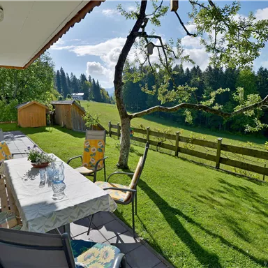 Ein einladender Außenbereich mit einem Tisch und Stühlen, umgeben von grünem Gras und einem schönen Ausblick auf die Landschaft. Im Hintergrund sind Bäume und ein kleiner Schuppen zu sehen.