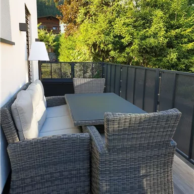 Ein gemütlicher Balkon mit einem modernen Rattan-Möbelset. Die grüne Umgebung sorgt für eine entspannte Atmosphäre.