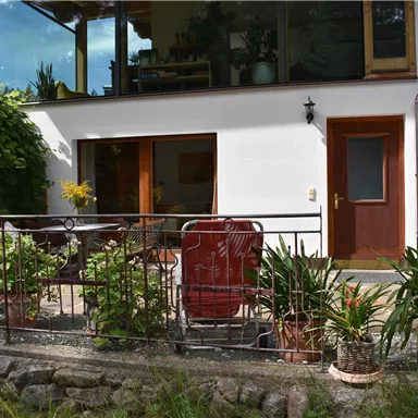 Ein schöner Wohnbereich mit einer Terrasse, die mit Pflanzen und Möbeln dekoriert ist. Ein roter Sonnenschirm sorgt für Schatten.