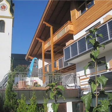 A modern building with wooden cladding and solar panels. In the background, there is a church tower under a clear sky.