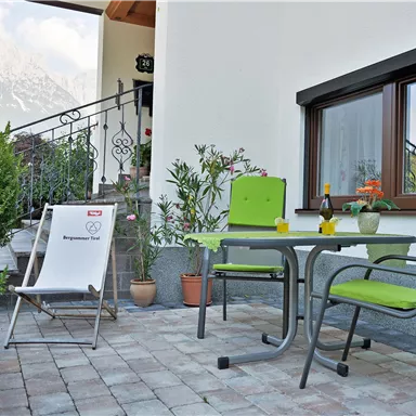 Eine gemütliche Terrasse mit einem Tisch und Stühlen in Grün. Im Hintergrund sind Pflanzen und die umliegenden Berge sichtbar.