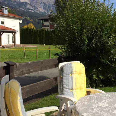 Ein schöner Garten mit zwei Liegestühlen und einem Tisch. Im Hintergrund sind Berge und ein klarer Himmel sichtbar.