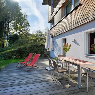 A beautiful terrace with a table and chairs, surrounded by greenery. Two lounge chairs invite relaxation.